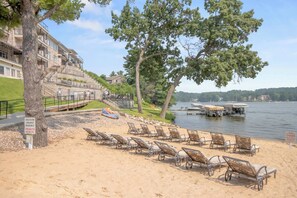 A beach with lounge chairs, a private beach sign, and a view of a lake with boats.