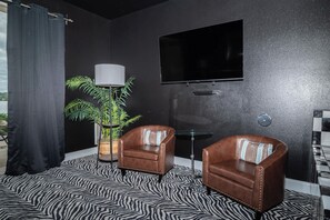 A room with two leather armchairs, a floor lamp, a television on the wall, and a zebra-patterned rug.