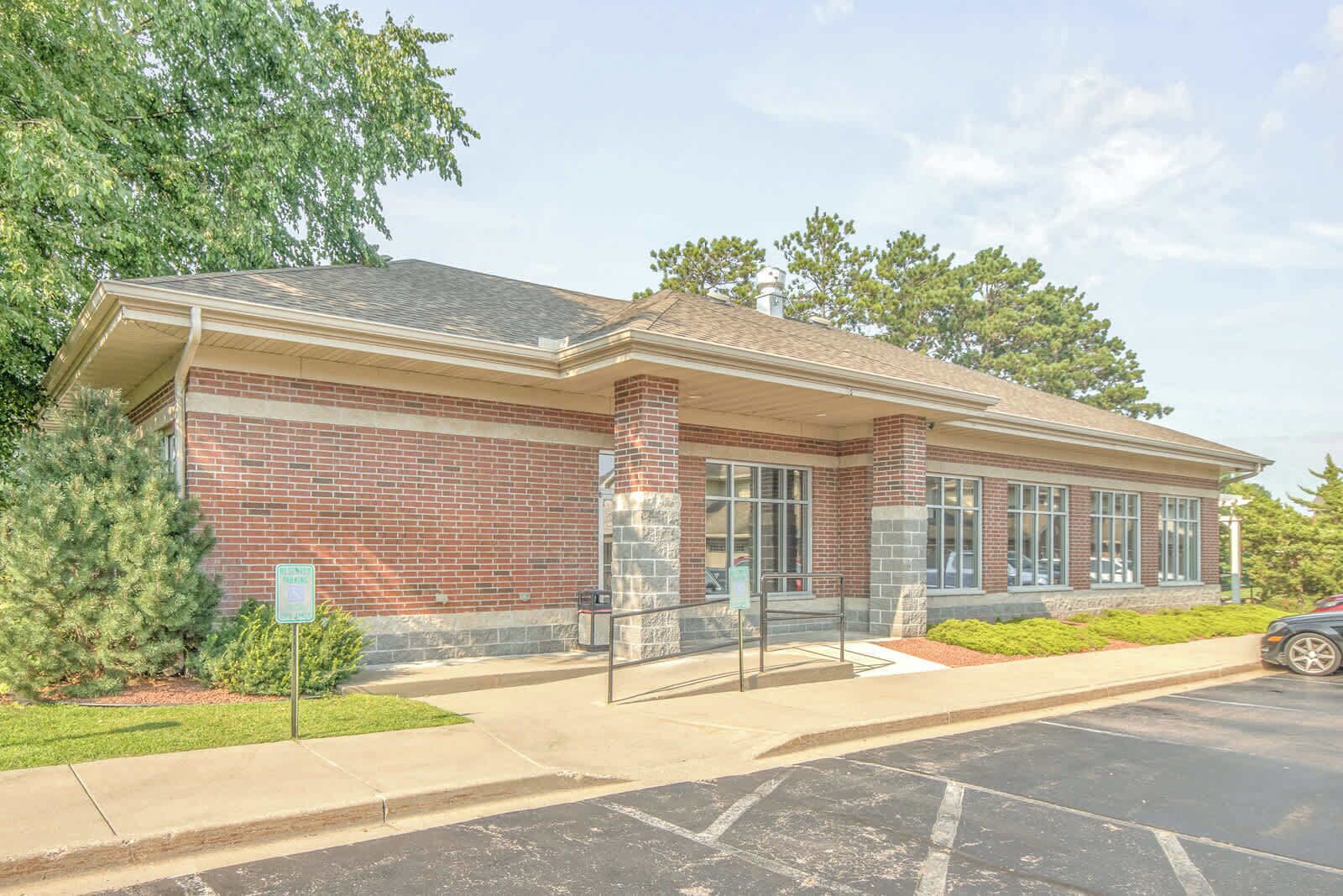 A brick building with a covered entrance, large windows, and a parking lot.