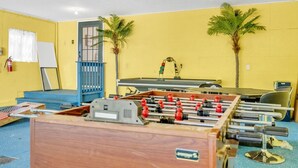 A room with a foosball table, a blue gate, two palm trees, and a whiteboard.