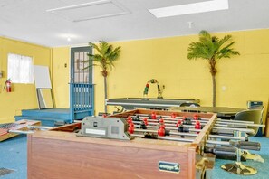 A room with a foosball table, a blue gate, two palm trees, and a whiteboard.