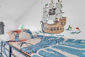 Un dormitorio con cama, almohadas y un mural de un barco pirata.
