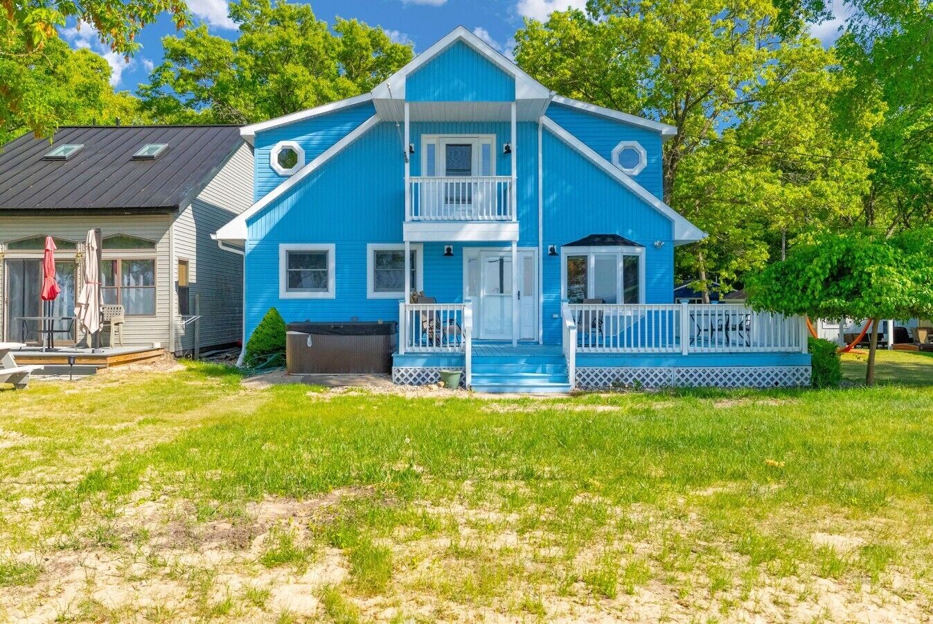 Een tweelaags huis met een blauwe gevel, een voortuin met een witte balustrade, en een klein terras.