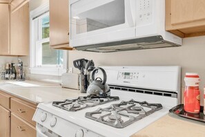 Cocina equipada con estufa a gas, hervidor y microondas.