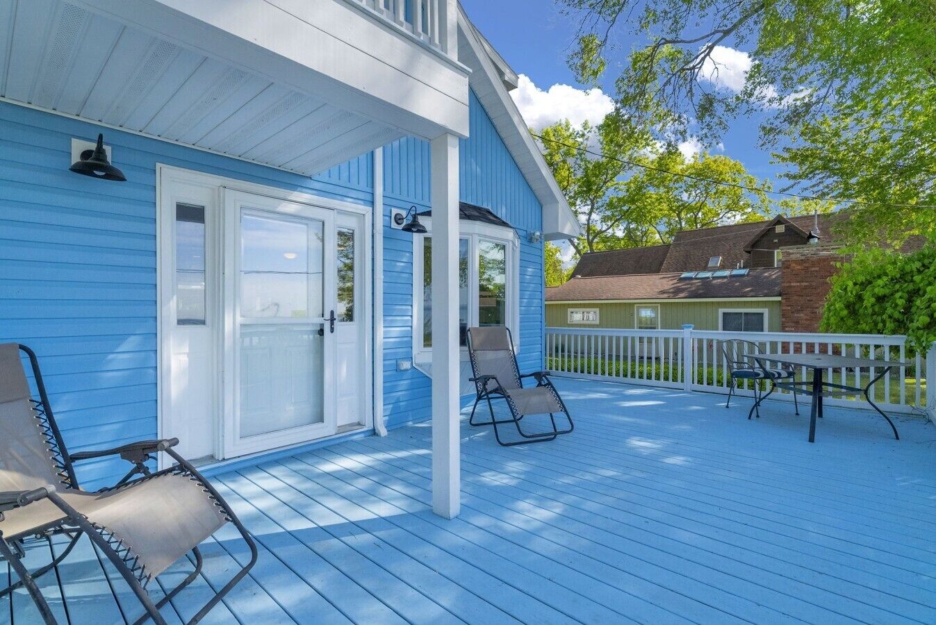 A blue house with a covered porch, two chairs, and a table.
