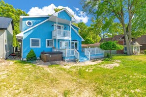 A two-story blue house with a balcony, a hot tub, and a fenced yard.