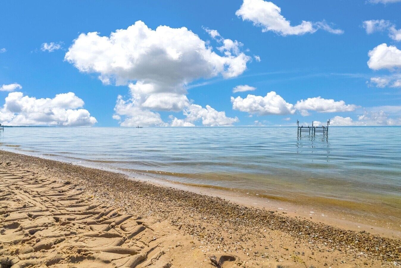 Een strand met heldere lucht, kalm water en een houten pier die in zee uitloopt.