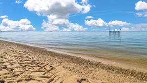 A beach with clear skies, calm water, and a wooden pier extending into the sea.