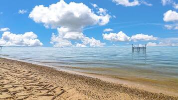 Een strand met heldere lucht, kalm water en een houten pier die in zee uitloopt.