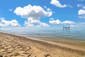 A beach with clear skies, calm water, and a wooden pier extending into the sea.