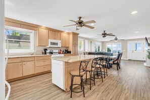 A modern kitchen with wooden cabinets, a central island with bar stools, and ceiling fans.