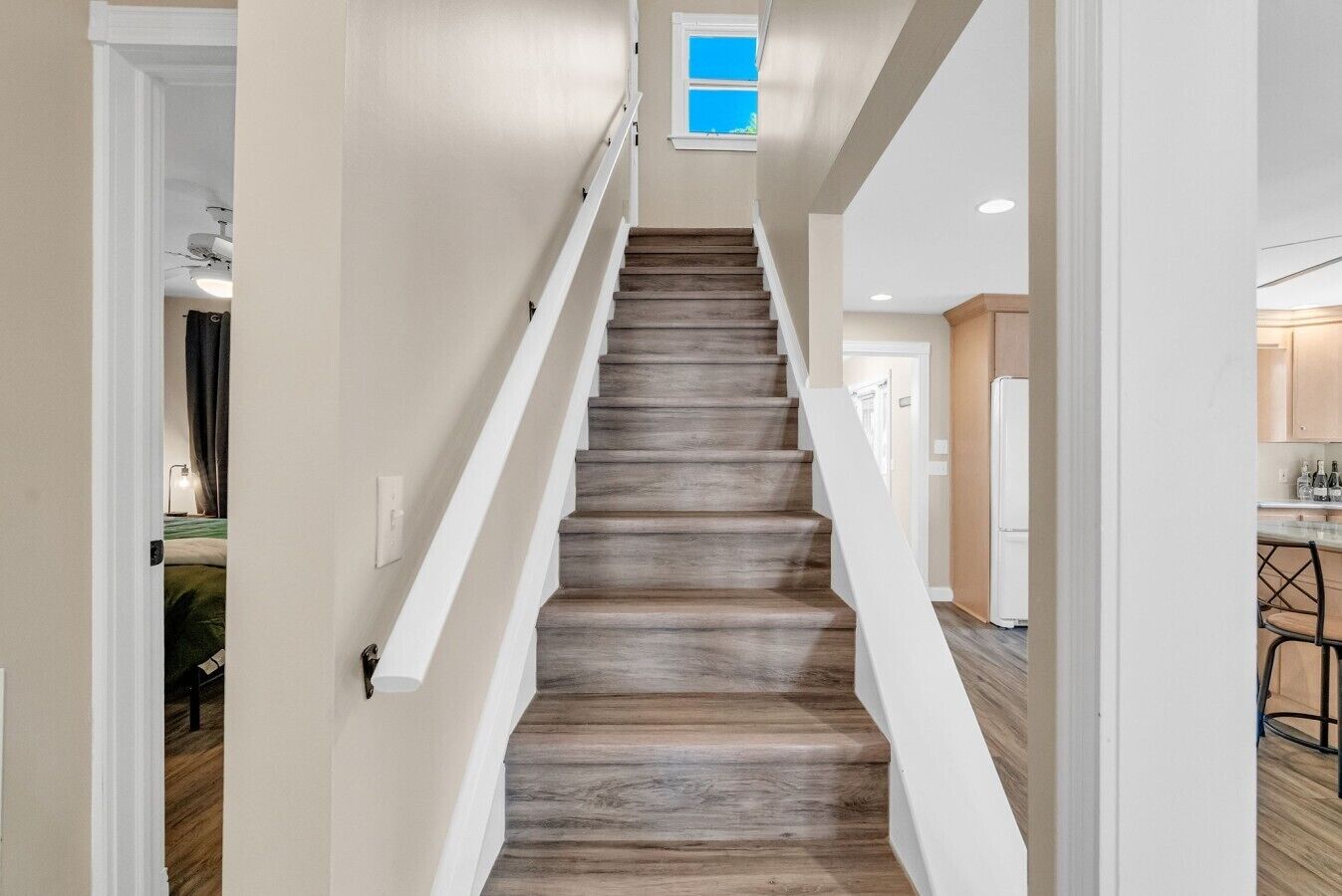Un escalier avec des marches en bois et une rampe blanche menant à une pièce comprenant un coin cuisine.
