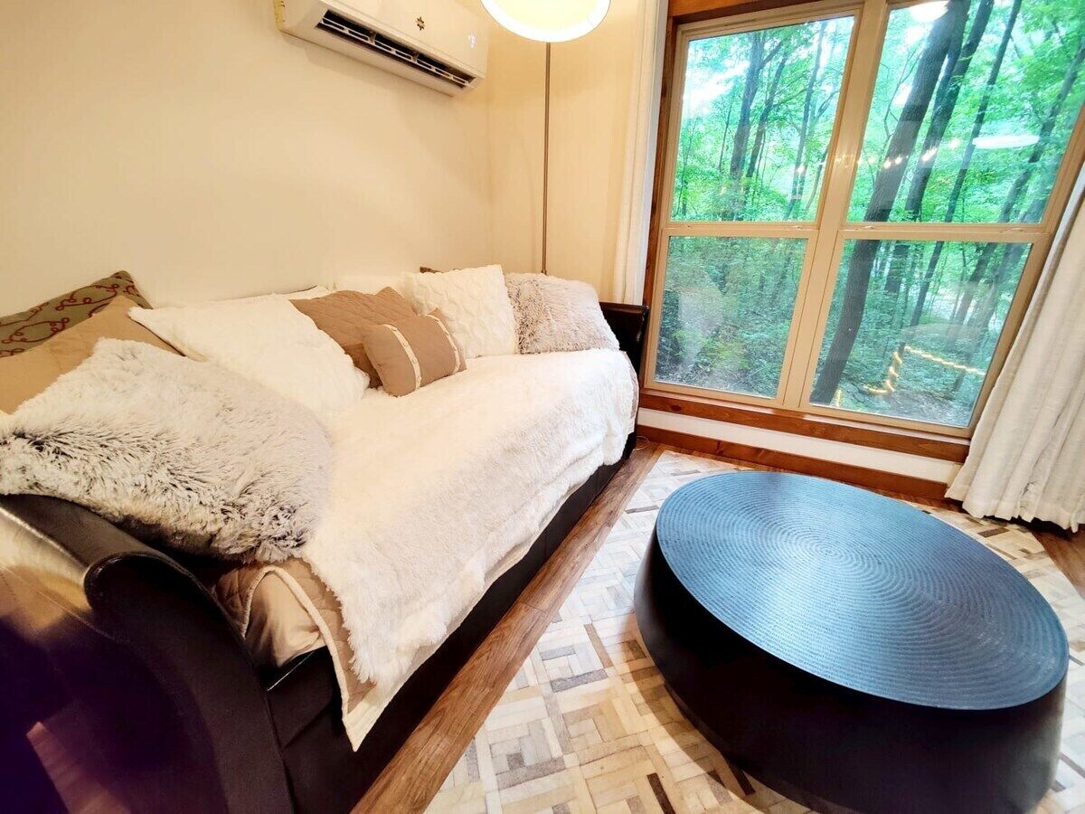 Een kamer met een bed, een ronde tafel en een raam met uitzicht op een bos.