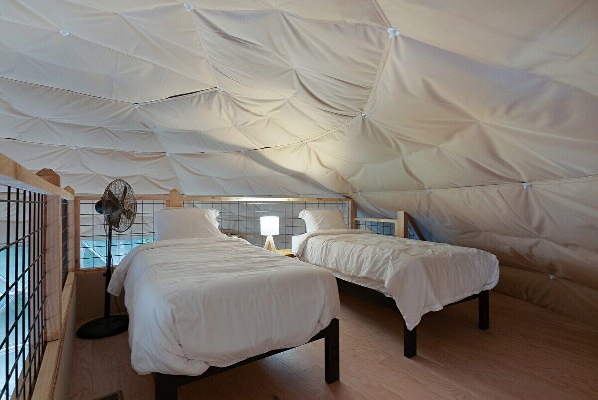 A tented room with two beds, a fan, and a window.