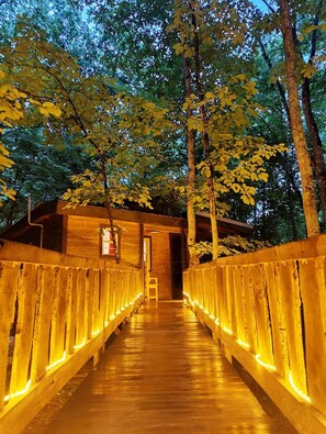 A wooden bridge with illuminated railings leading to a building with a door and a sign.