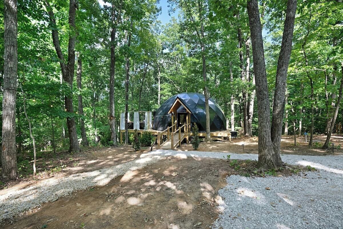 A dome-shaped tent in a forested area with a gravel path leading to it.