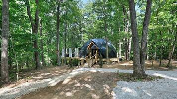 A dome-shaped tent in a forested area with a gravel path leading to it.