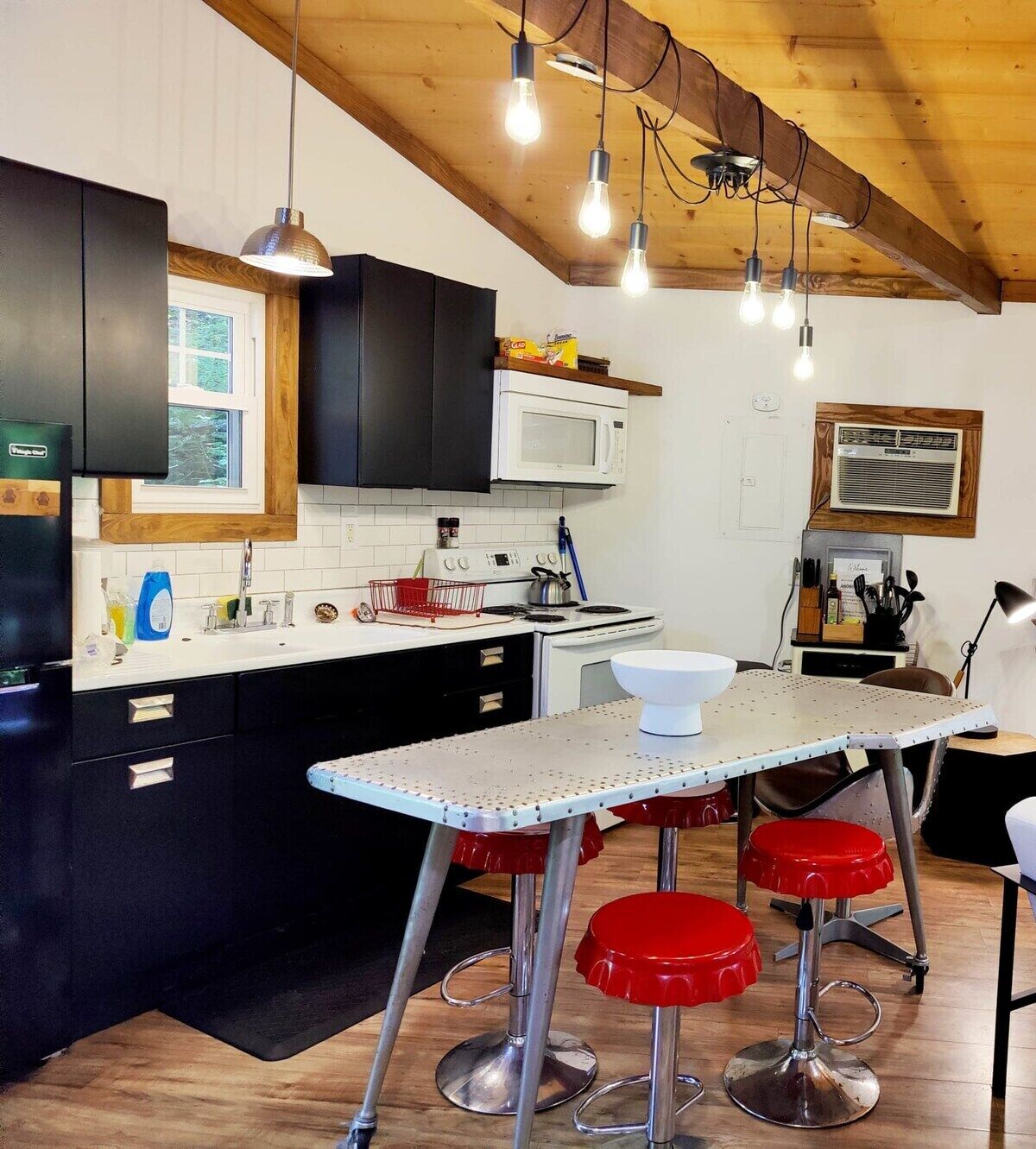 A modern kitchen with black cabinets, a white countertop, and a bar area with red stools.