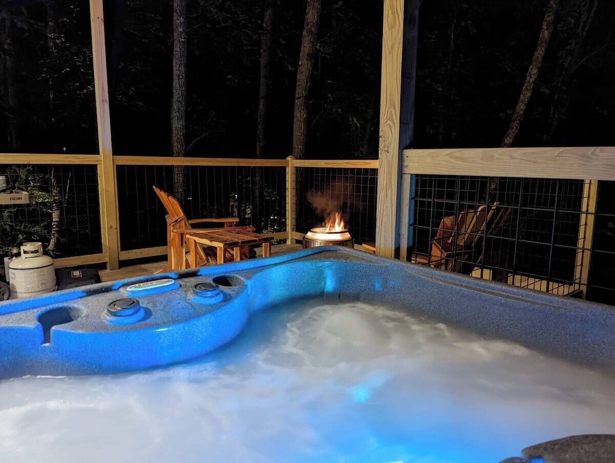 A hot tub with a wooden deck and a table, surrounded by trees.