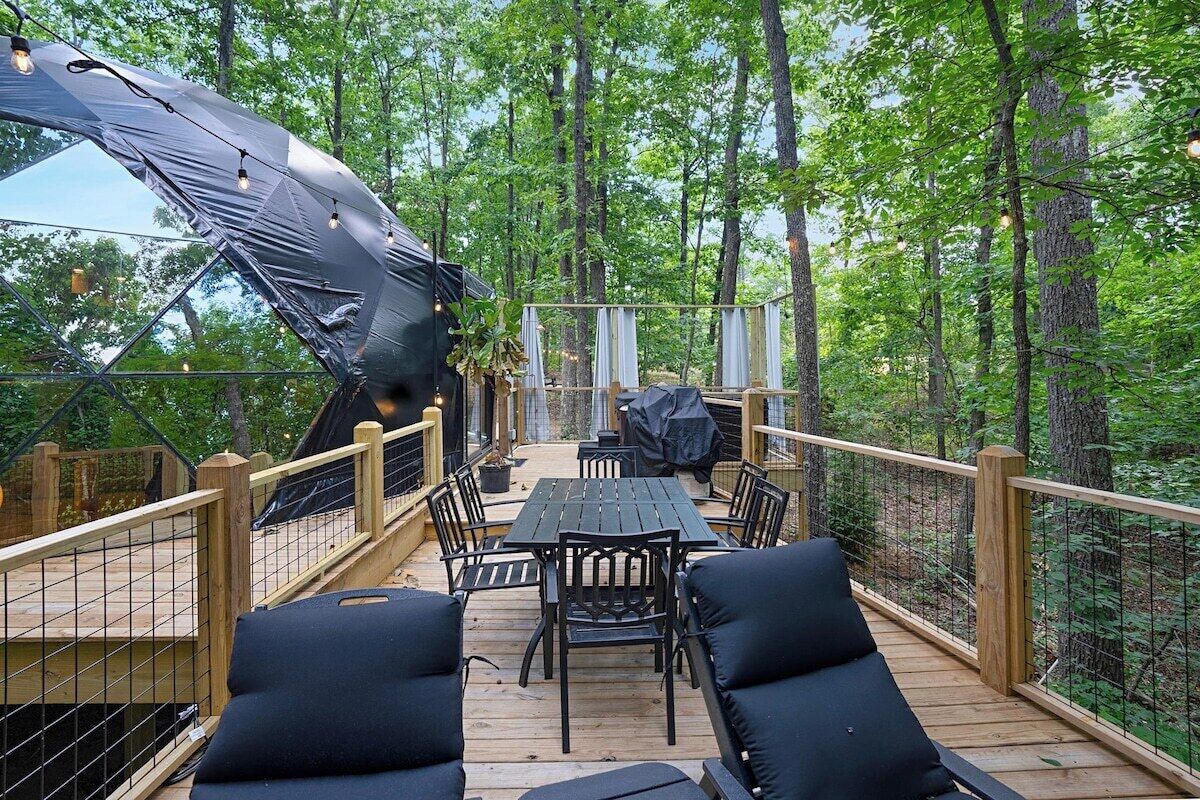 A wooden deck with a table and chairs, surrounded by a forest.