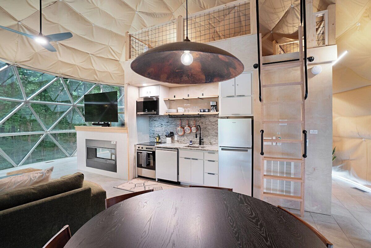 A modern kitchen with a large dining table, built-in appliances, and a view through large windows.