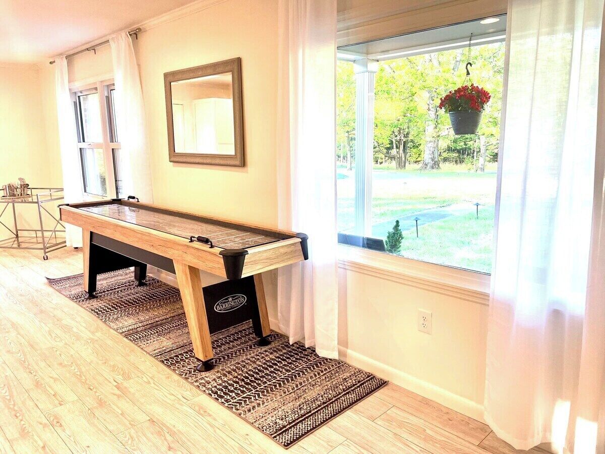 A pool table in a room with a view of a garden through a window.