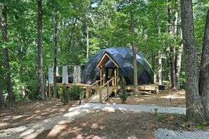 Tienda con forma de cúpula, un suelo de madera y escaleras, rodeada por un bosque.