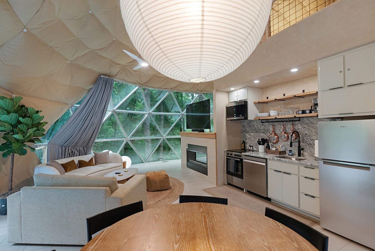 A modern kitchen with stainless steel appliances, a dining area with a wooden table, and a large window with a geometric view.