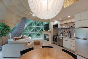 Eine moderne Küche mit Edelstahlgeräten, ein Essbereich mit Holztisch und ein großes Fenster mit geometrischer Aussicht.