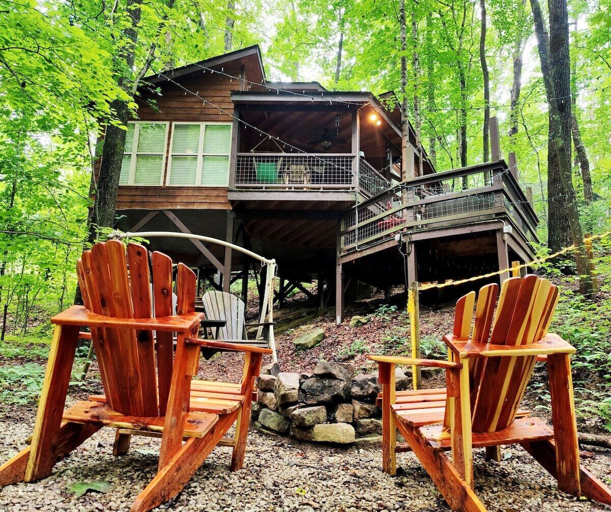 A cabin with a deck, two Adirondack chairs, and a stone fire pit.