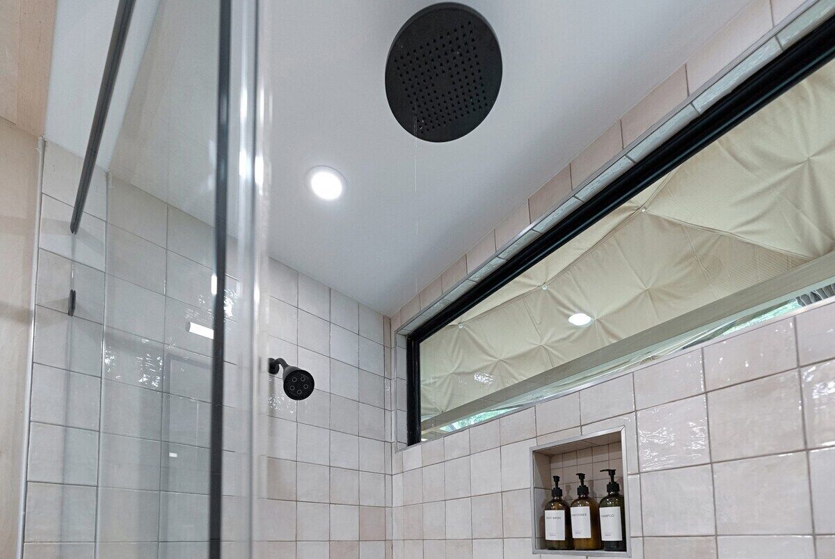 Un baño con cabina de ducha de vidrio, ducha con rociador en el techo y un estante con artículos de tocador.