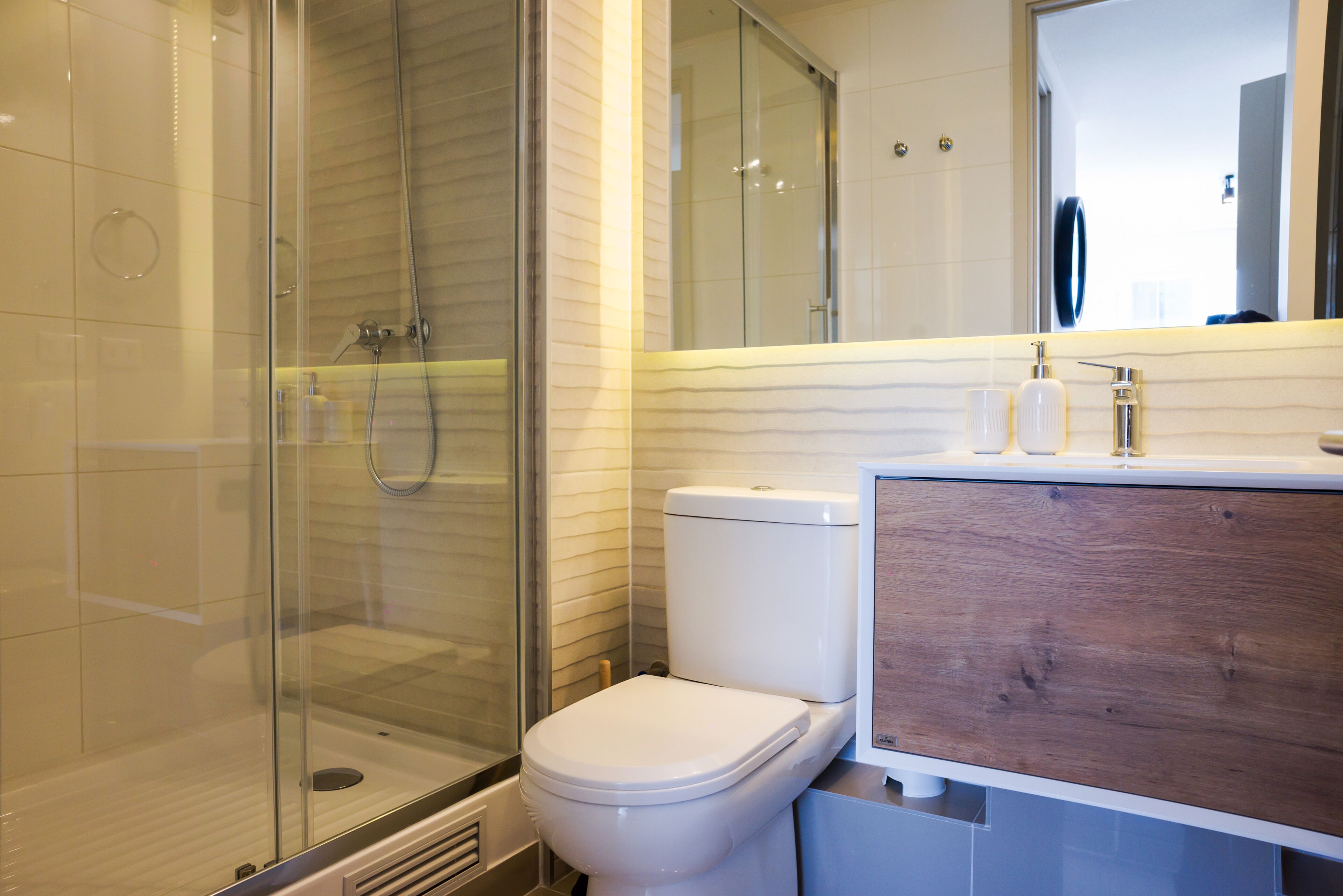 A modern bathroom with a glass shower enclosure, a white toilet, and a wooden vanity with a mirror.