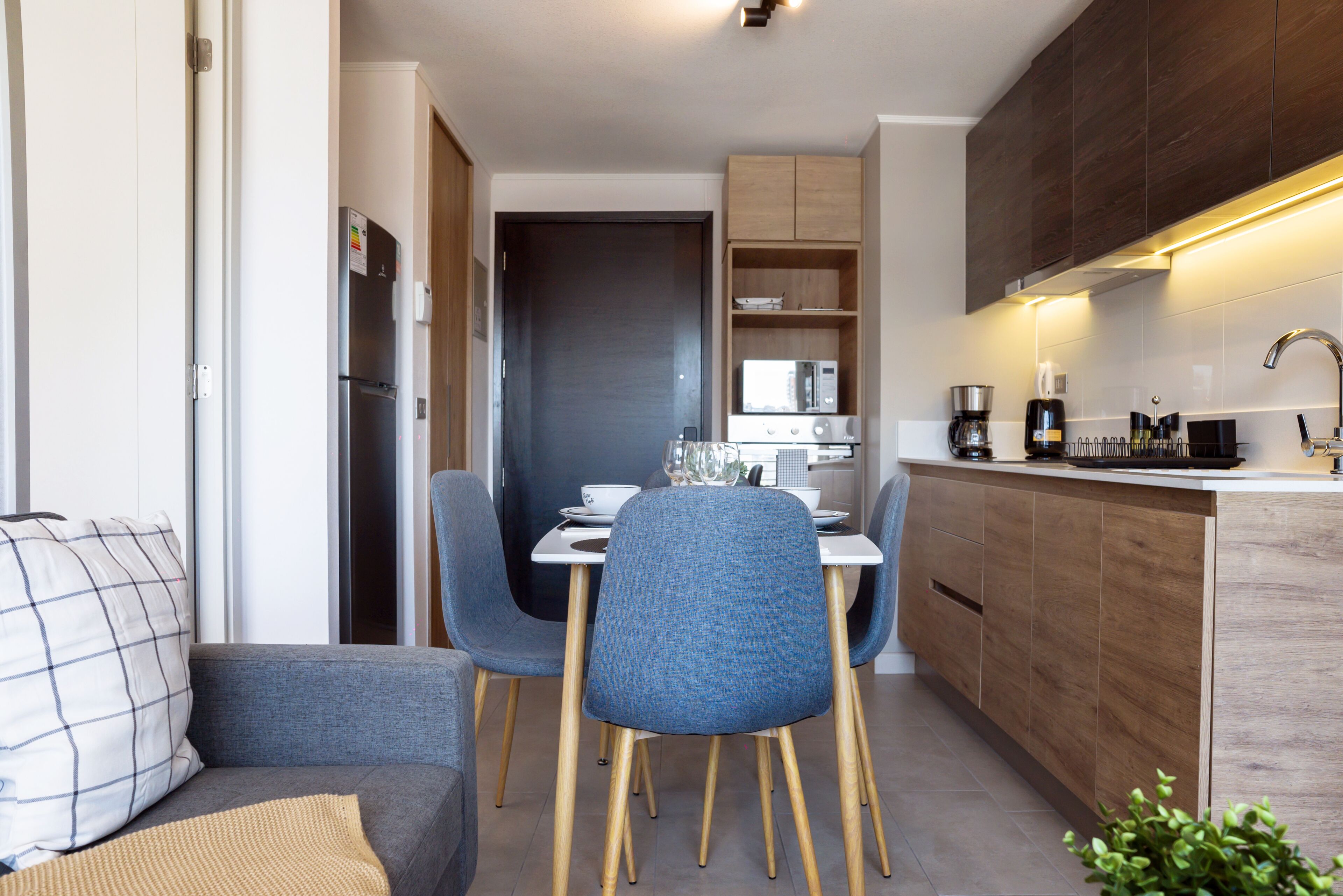 Une cuisine compacte dotée d’appareils électroménagers modernes, un coin repas avec une table et des chaises, et un espace salon confortable avec un canapé.