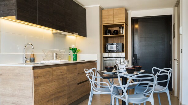 Una cocina moderna con una isla central, sillas blancas y una puerta de madera oscura.