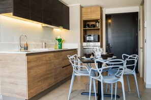 A modern kitchen with a central island, white chairs, and a dark wooden door. - Vicuña Mackenna Apartments By Andes STR (Ñuñoa)