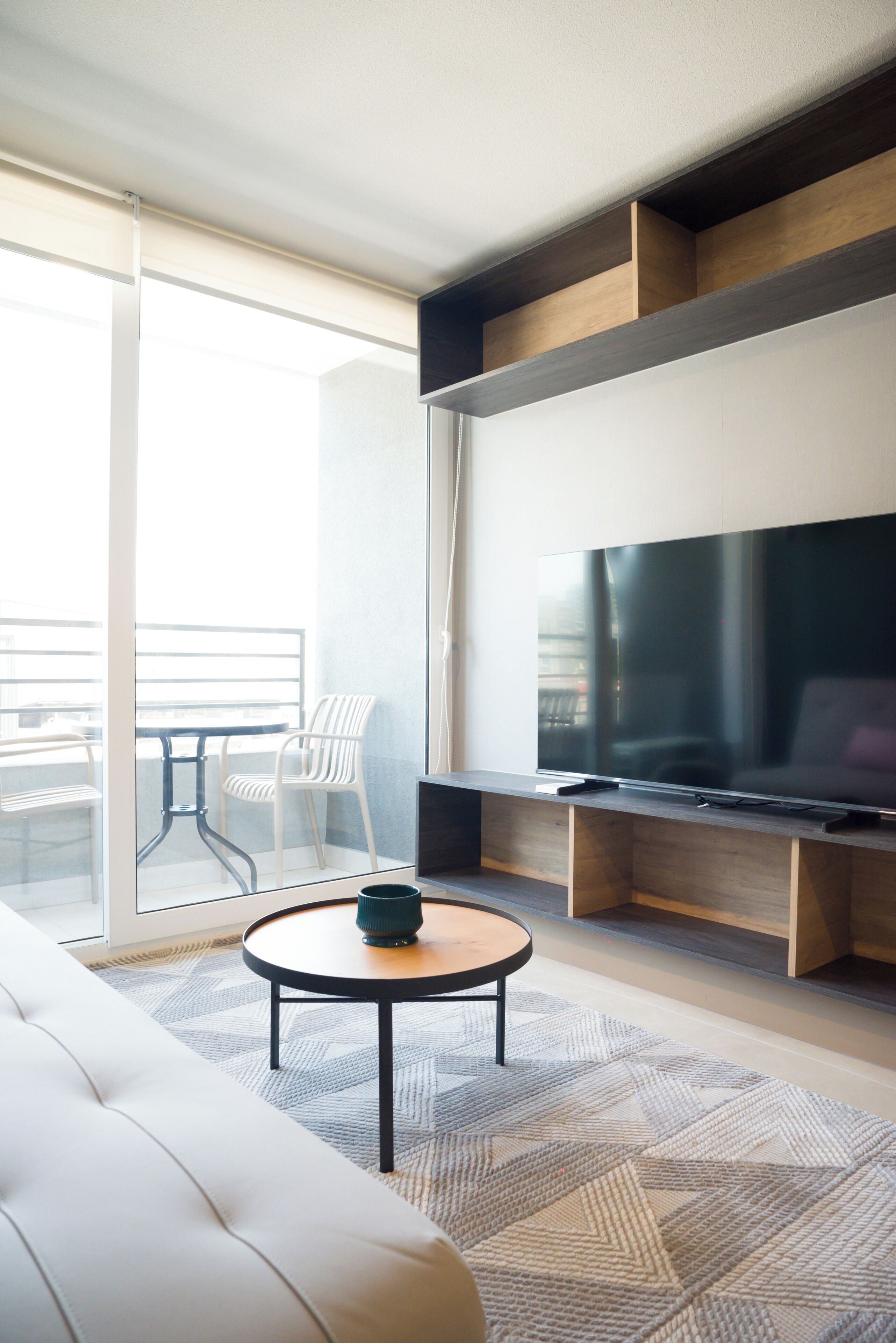 Een moderne woonkamer met een flatscreen televisie, een bank, een salontafel en een balkon met een glazen deur.