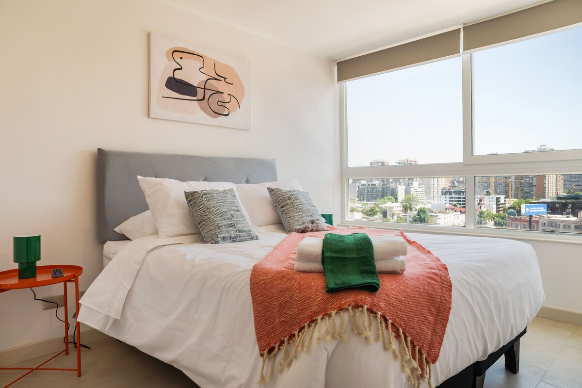 Ein modernes Hotelzimmer mit einem großen Bett, Blick auf die Stadt und schlichter Einrichtung.