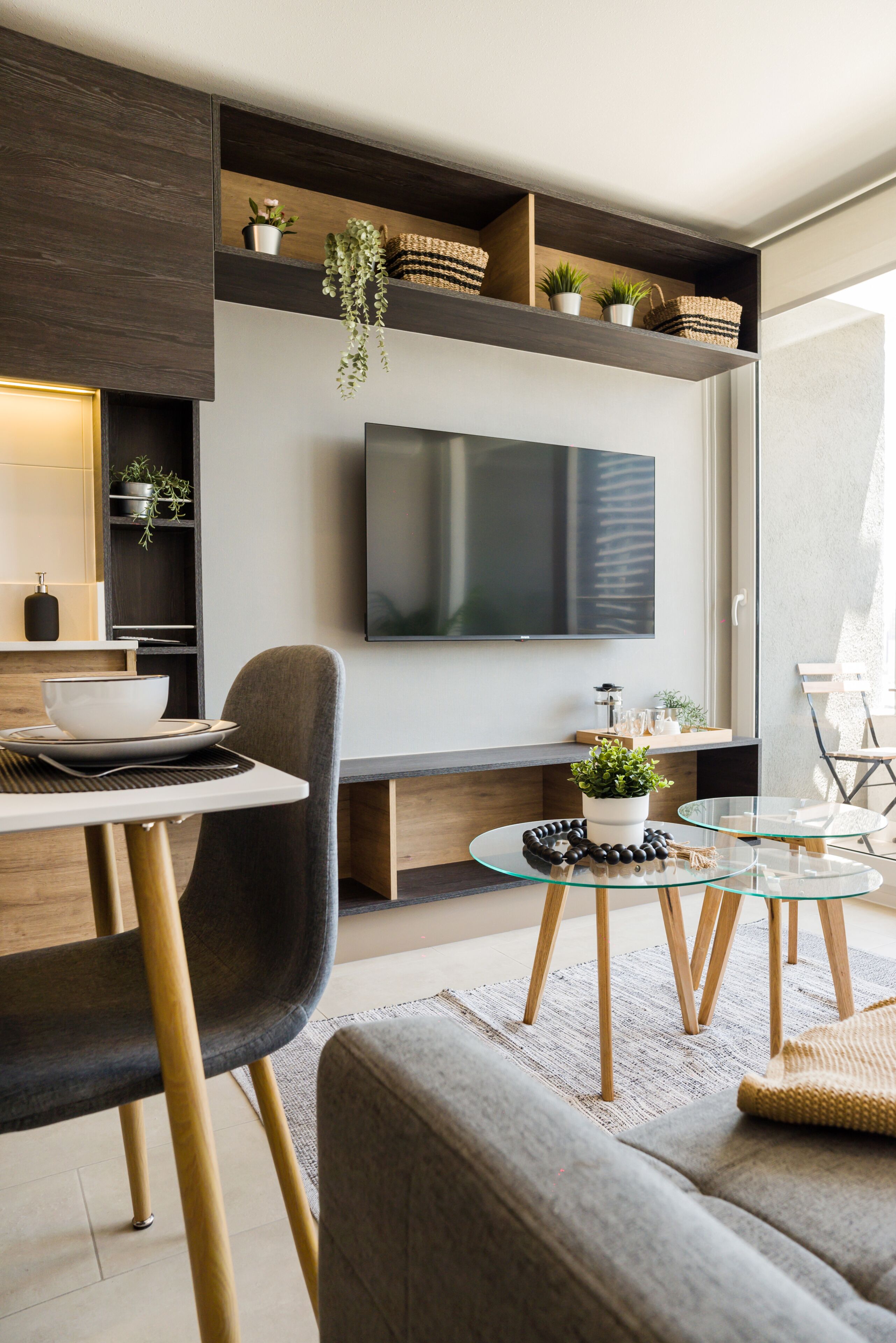A modern living room with a flat-screen TV mounted on the wall, a dining area with a table and chairs, and a seating area with a glass coffee table.