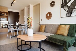 A modern living room with a round table, a sofa with cushions, and a decorative wall piece. - Vicuña Mackenna Apartments By Andes STR (Ñuñoa)