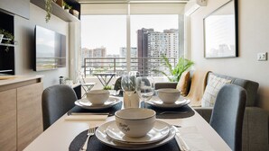 Comedor con una mesa dispuesta para dos, vistas urbanas a través de amplios ventanales y muebles modernos.