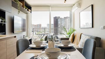 Comedor con una mesa dispuesta para dos, vistas urbanas a través de amplios ventanales y muebles modernos.