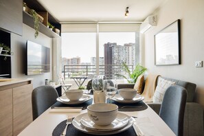Ein Essbereich mit Tisch für zwei Personen, Stadtblick durch große Fenster und moderne Möbel.