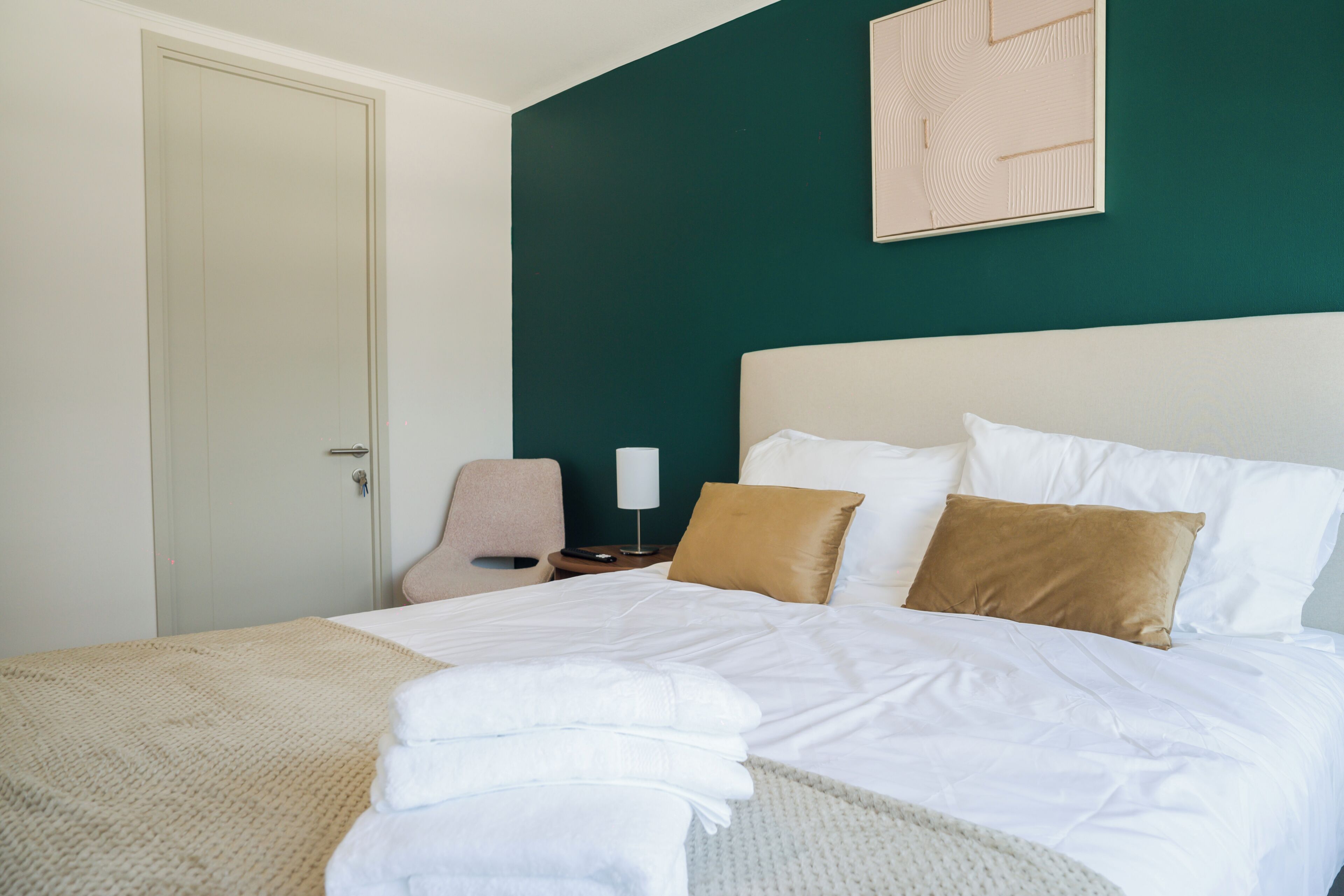 A hotel room with a bed, a chair, a nightstand, and a door.