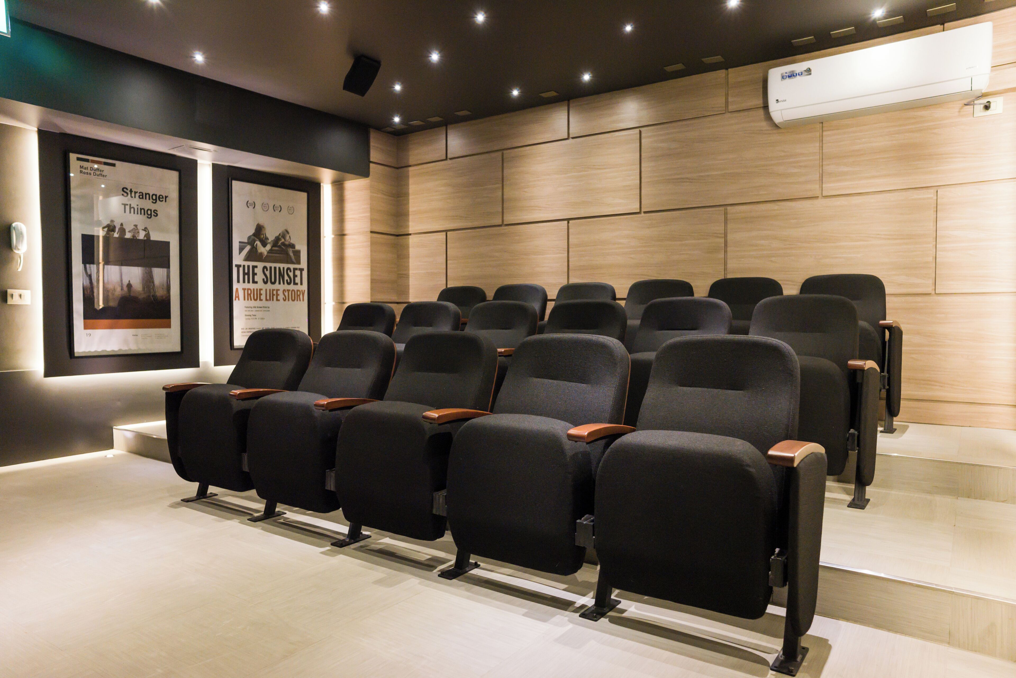 Une salle de cinéma avec des rangées de sièges noirs, un mur en bois et deux affiches accrochées au mur.
