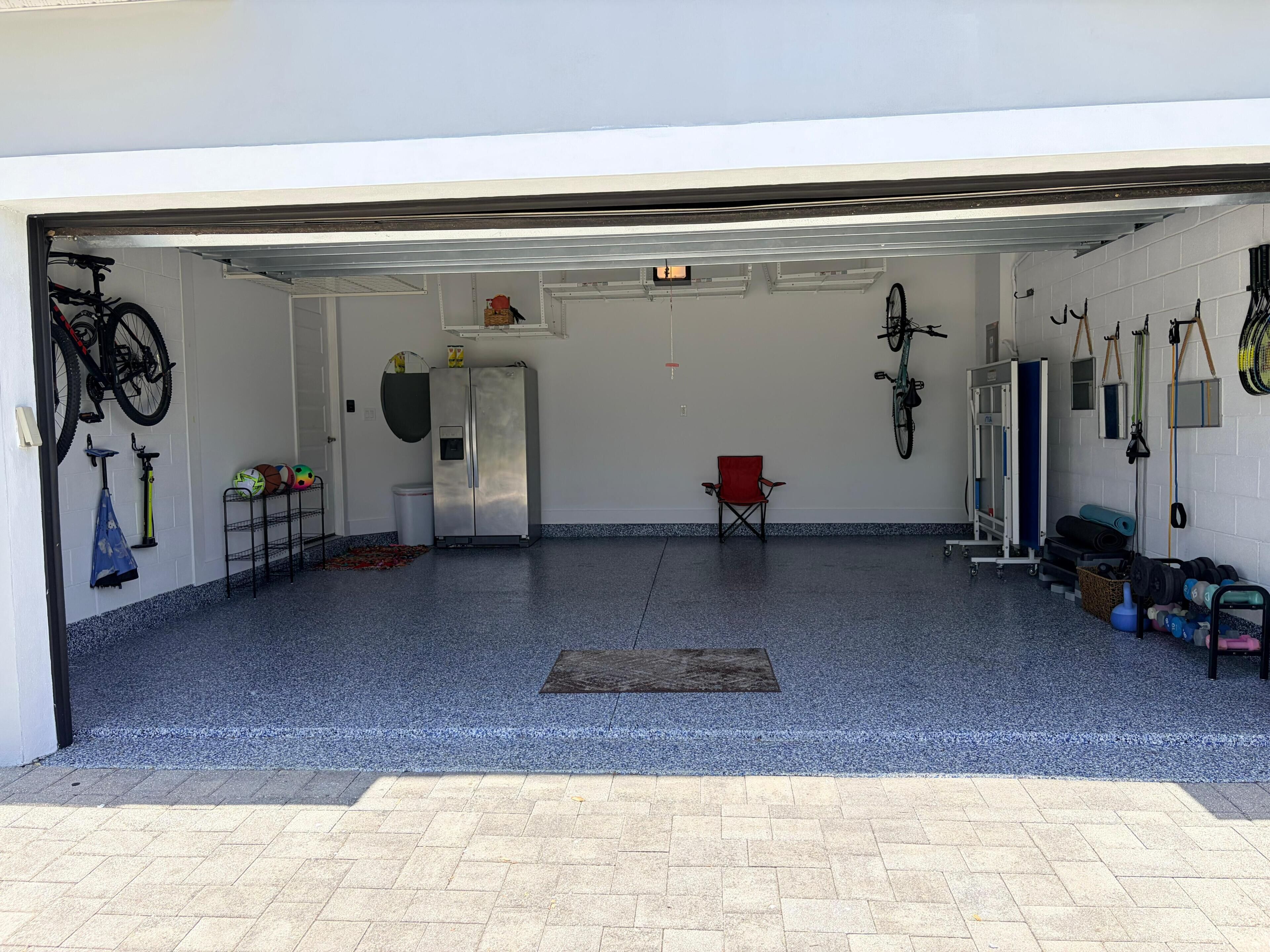 Een garage met een blauwe vloer, een rode stoel en diverse sportattributen, waaronder fietsen en gewichten.