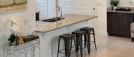 A modern kitchen with a central island, bar stools, pendant lighting, and a decorative wall piece.
