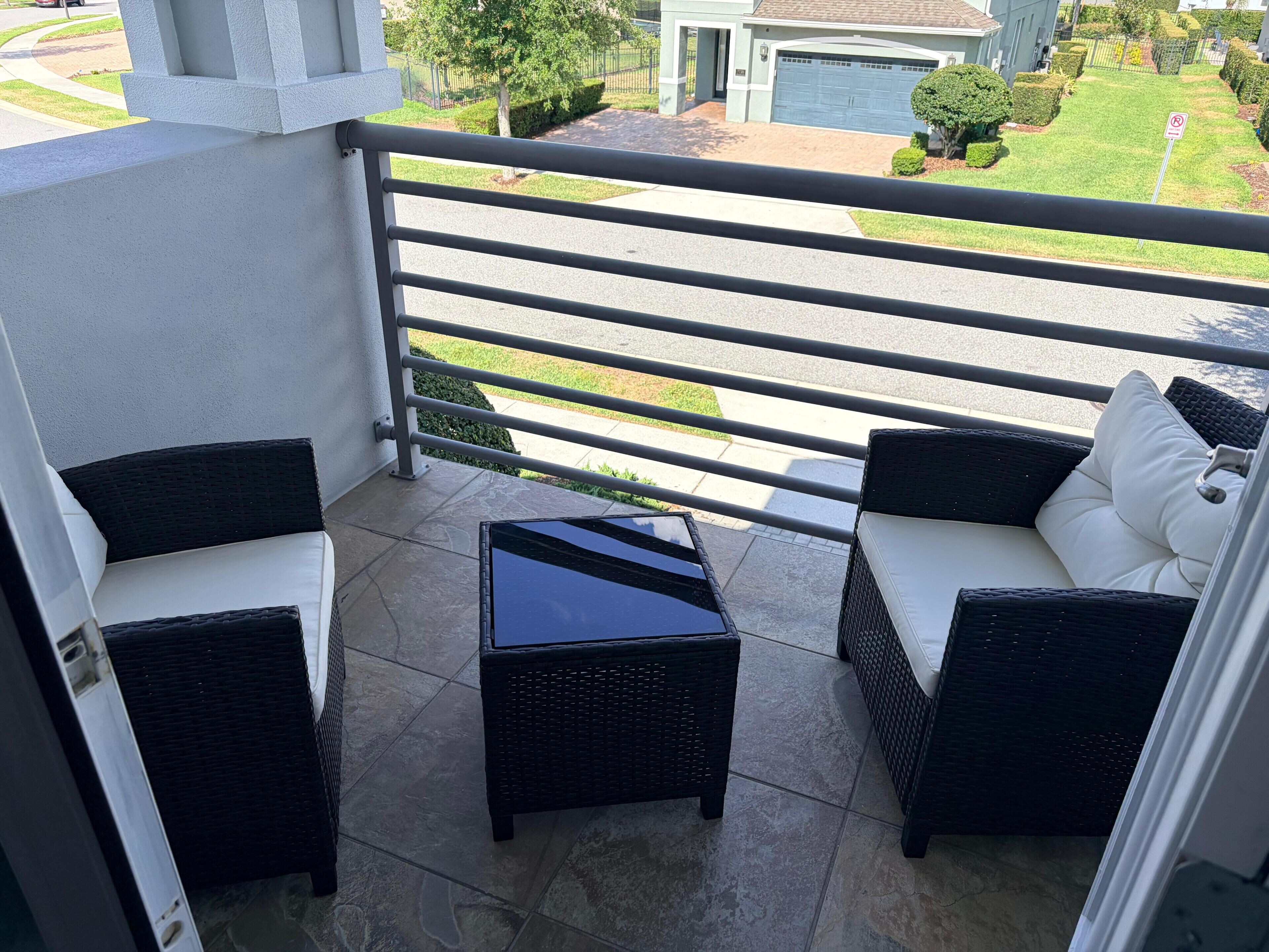 A balcony with wicker furniture and a glass table, overlooking a residential street.