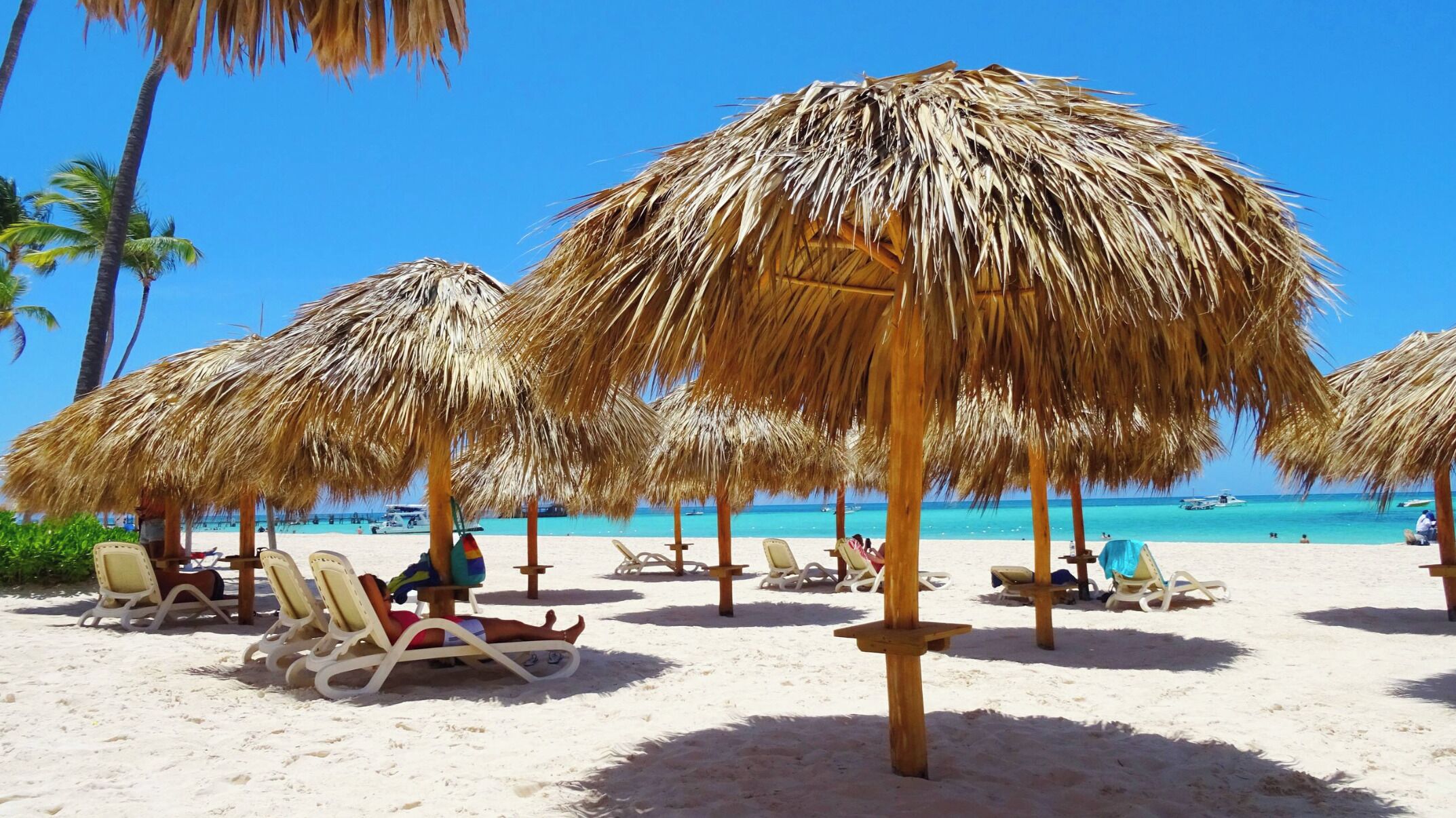 Ein Strand mit reetgedeckten Sonnenschirmen und Liegestühlen.