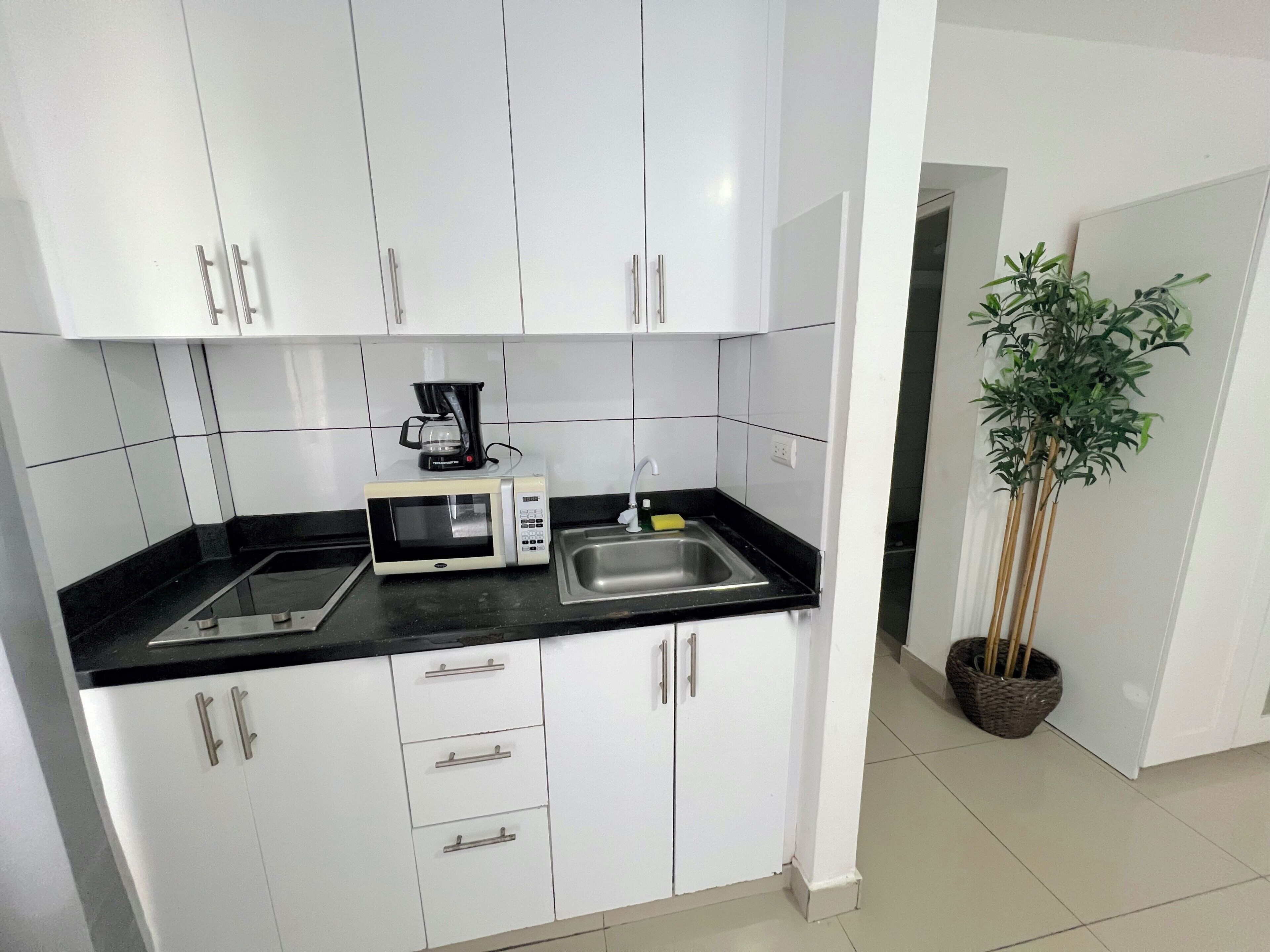 A kitchen with white cabinets, a microwave, a coffee maker, and a sink.