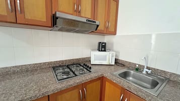 Una cocina con alacenas de madera, estufa a gas, microondas y pileta de acero inoxidable.